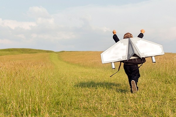 Child playing in field with plane wings on back