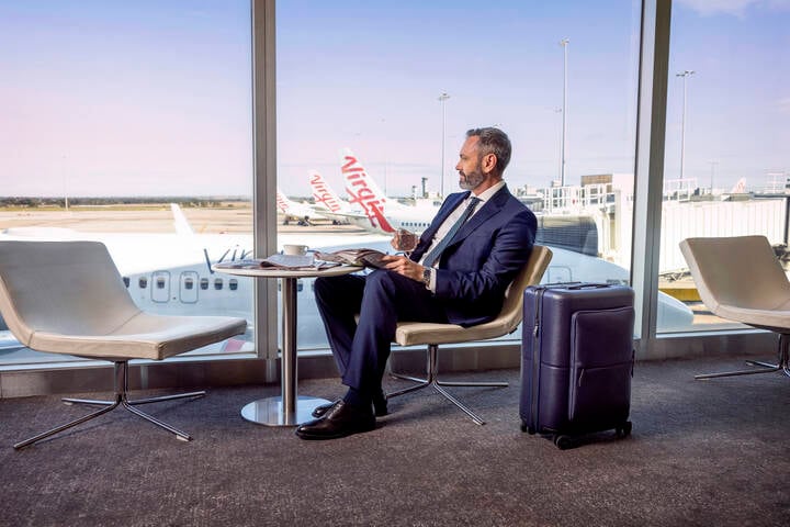 Businessman seated comfortably in the Virgin Australia lounge, reading a newspaper during his business trip
