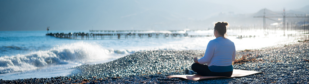 Woman sitting on the mat at the seashore having view on the big wave and  jetty