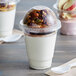 A clear plastic Choice cup filled with yogurt and granola with a red and white lid on a table.