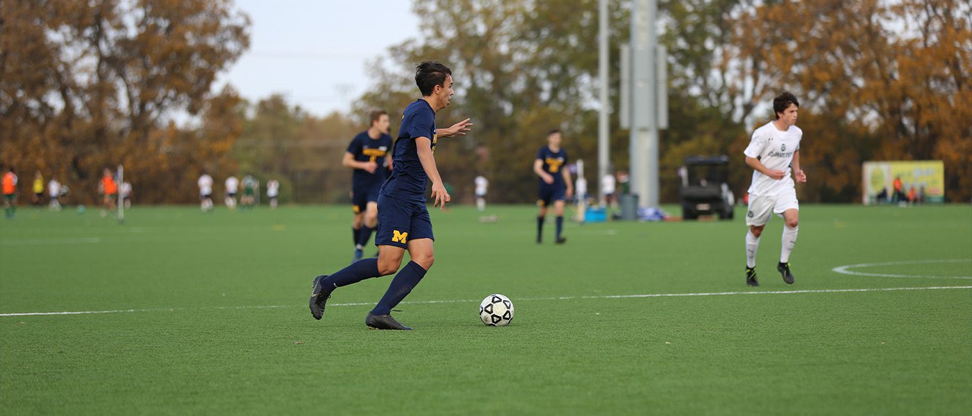 soccer player dribbling the ball in the middle of a field with other players in the background