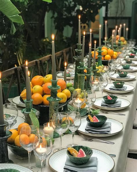 a long table is set with plates, glasses and candles for an outdoor dinner party