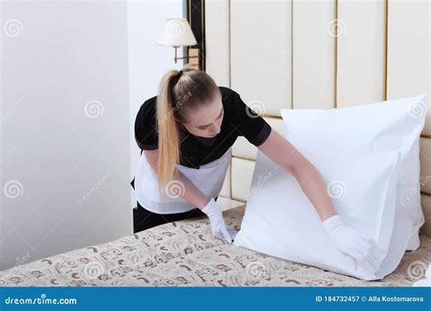 Cleaning in a Hotel Room.a Uniformed Maid with White Gloves Adjusts the Pillows on the Bed Stock ...