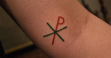 Minimalist Chi Rho symbol tattoo on the inner arm.