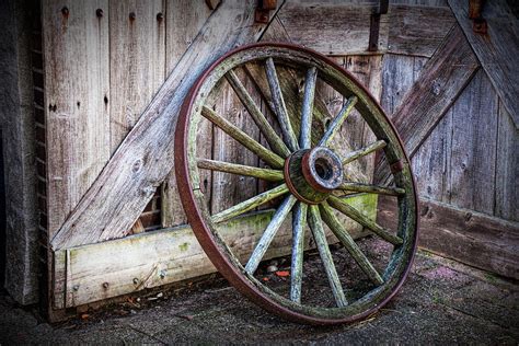 Old Rustic Wooden Wagon Wheel leaning against an old Barn Door Photograph by Randall Nyhof