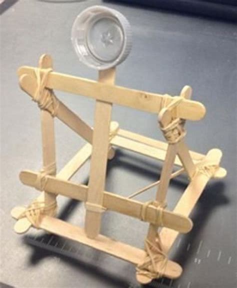 A photograph shows a small catapult structure made from Popsicle sticks rubber bands and a ...