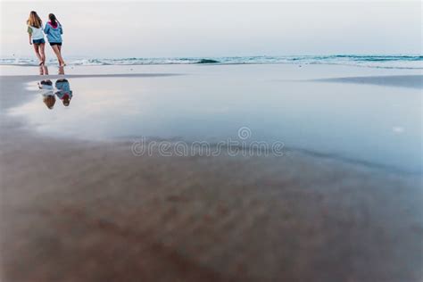 Two Friends Walking at Sunset on a Beach, Reflecting in the Puddles of Sand Stock Image - Image ...