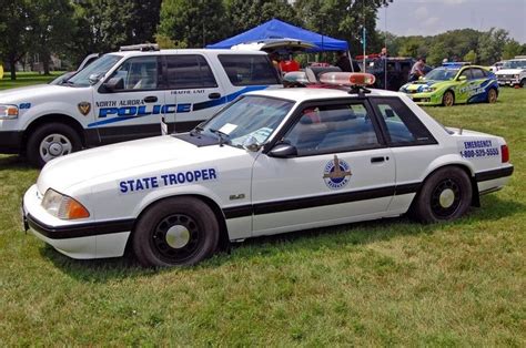 two police cars parked next to each other in the grass with tents and trees behind them