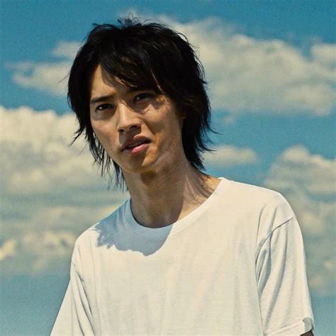 a man with black hair standing in front of clouds