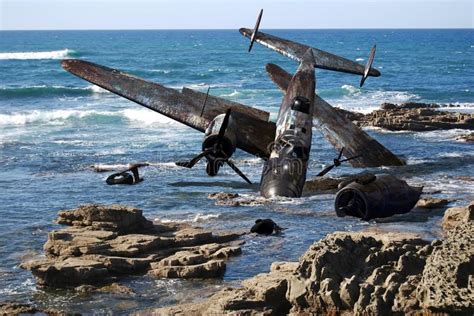 an old plane sitting on top of rocks in the water near the ocean with waves crashing around it