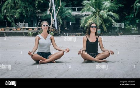 Two girlfriends doing yoga pose on beach in summertime in lotus position. Spiritually concept ...