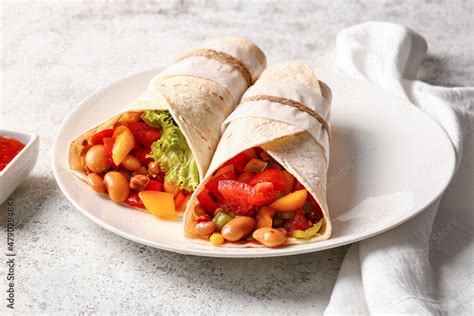 Plate of tasty Mexican burritos with vegetables on light background Stock Photo | Adobe Stock