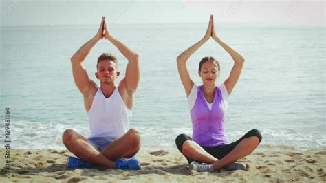 Smiling couple practising yoga poses sitting on beach by sea at daytime Stock Video | Adobe Stock