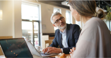 A man and woman sit at a desk with a laptop computer.