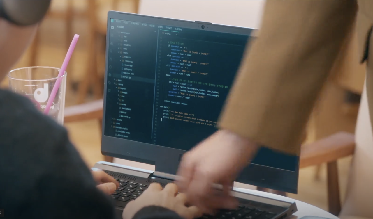 screenshot of a scene from the kdrama "no gain no love". it is a shot of hajun's laptop screen, which has visual studio code open. some code is on that screen, though small and not very visible. hajun's hands are on the keyboard, typing, and a hand from someone else standing off screen is reaching over to press a key on the keyboard.