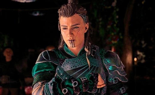 Image ID: screenshot from the Ubisoft game Assassin's Creed Valhalla, featuring the female version of the playable protagonist character Eivor. She is White & ethnically Norse wearing green metal armor, with a long scar on her cheek & a partially shaved with pulled back into a ponytail. Tattoos of 3 thick lines extend down her chin, similar to the photo of the Inuk woman in the first image. End ID