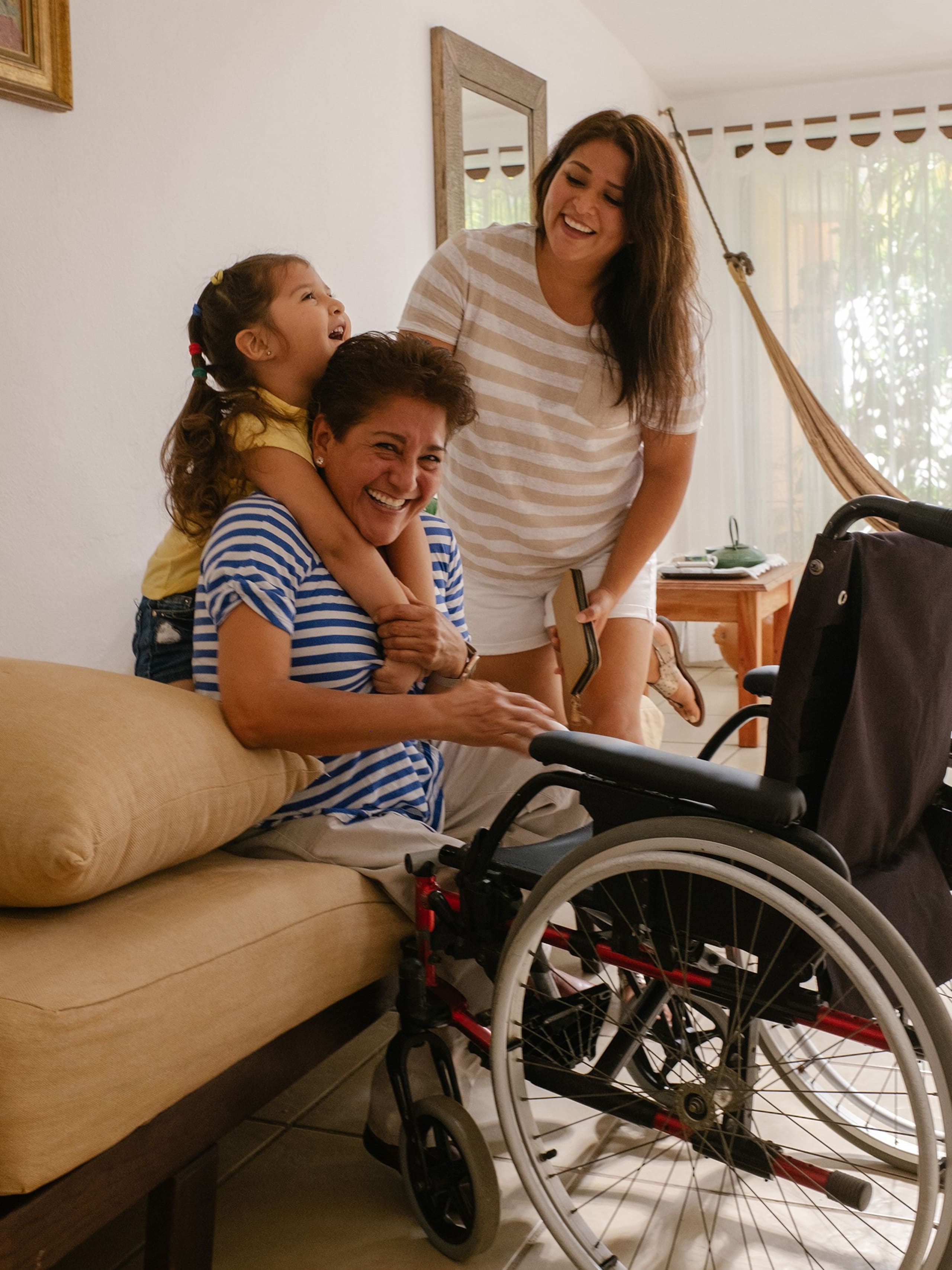 Tres generaciones de una familia sonríen y se ríen en un alojamiento accesible de Airbnb. Frente a ellos, la persona de mayor edad está sentada en una silla de ruedas.