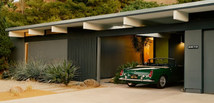 A photo shows the exterior of a single-level desert home with a covered parking spot containing a vintage convertible sports car.