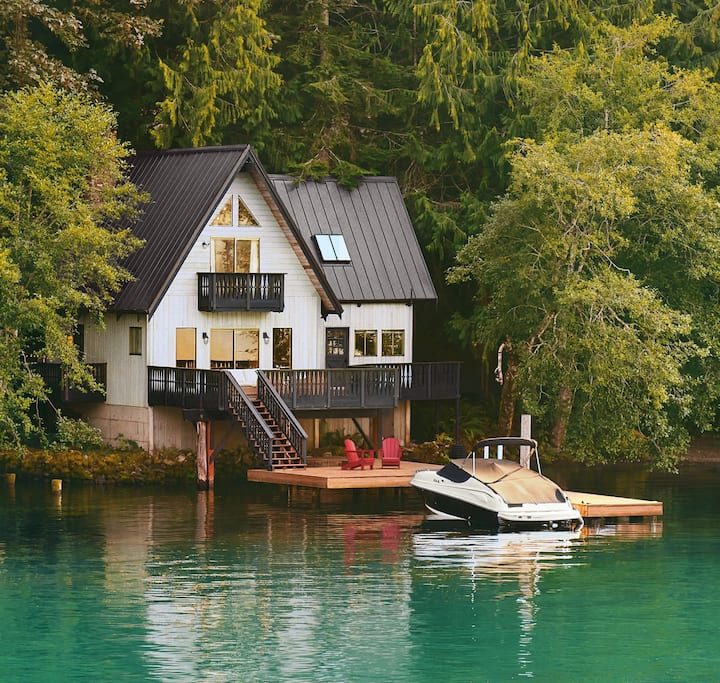 A photo shows a boat, covered and docked in front of a 2-story home on the edge of a lake.