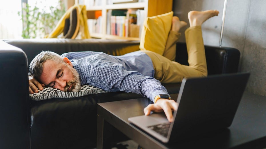 man sleeping with hand on laptop keyboard at home