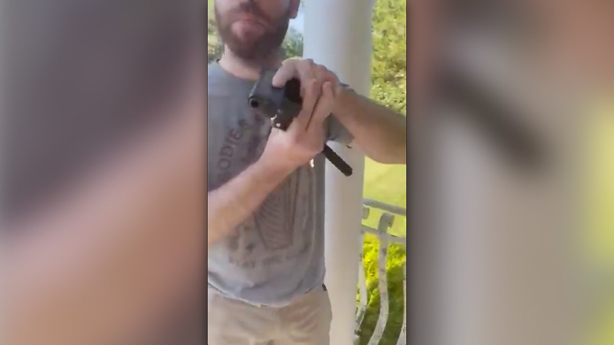 Man in gray T-shirt aims handgun at camera