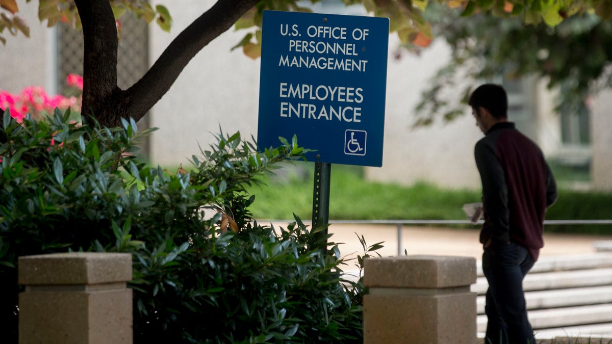 Letting more Americans work from home would open up government jobs all across the US. FILE: A man walks past an employees entrance sign outside the Theodore Roosevelt Building, headquarters of the U.S. Office of Personnel Management in Washington, D.C. on Friday, June 5, 2015. 