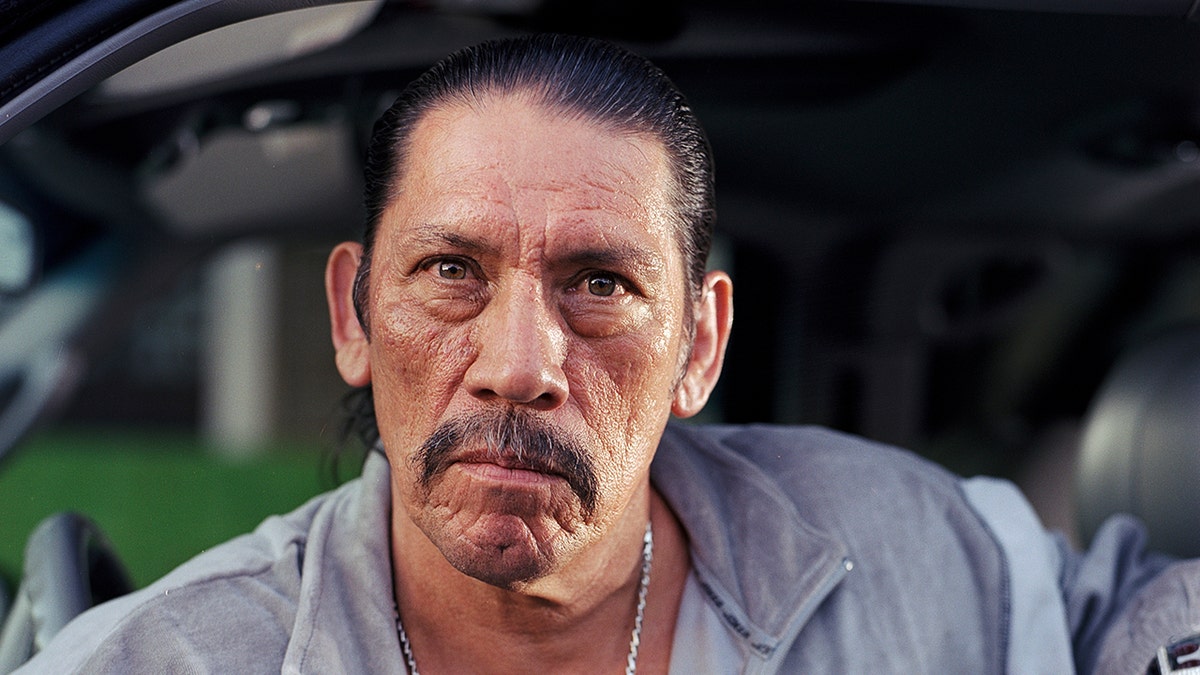 Danny Trejo looks serious into the camera in a picture wearing grey