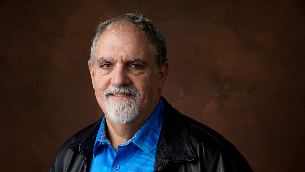 Jon Landau smiling in a black jacket and bright blue shirt