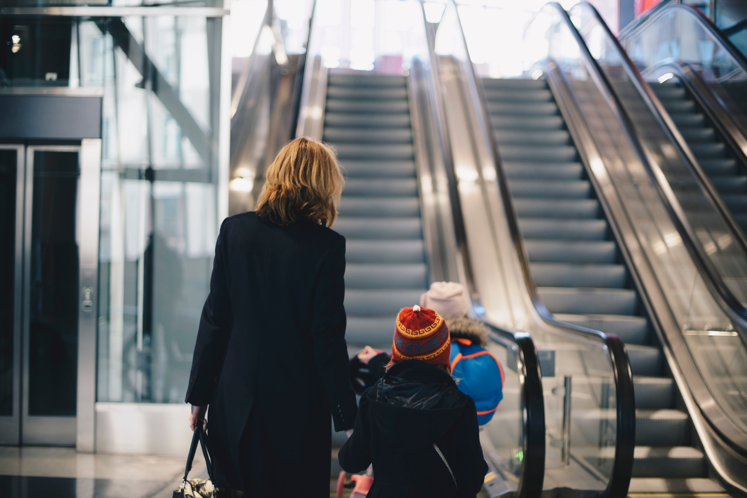 Rear view of mother and daughters walking towards escalator at railroad station