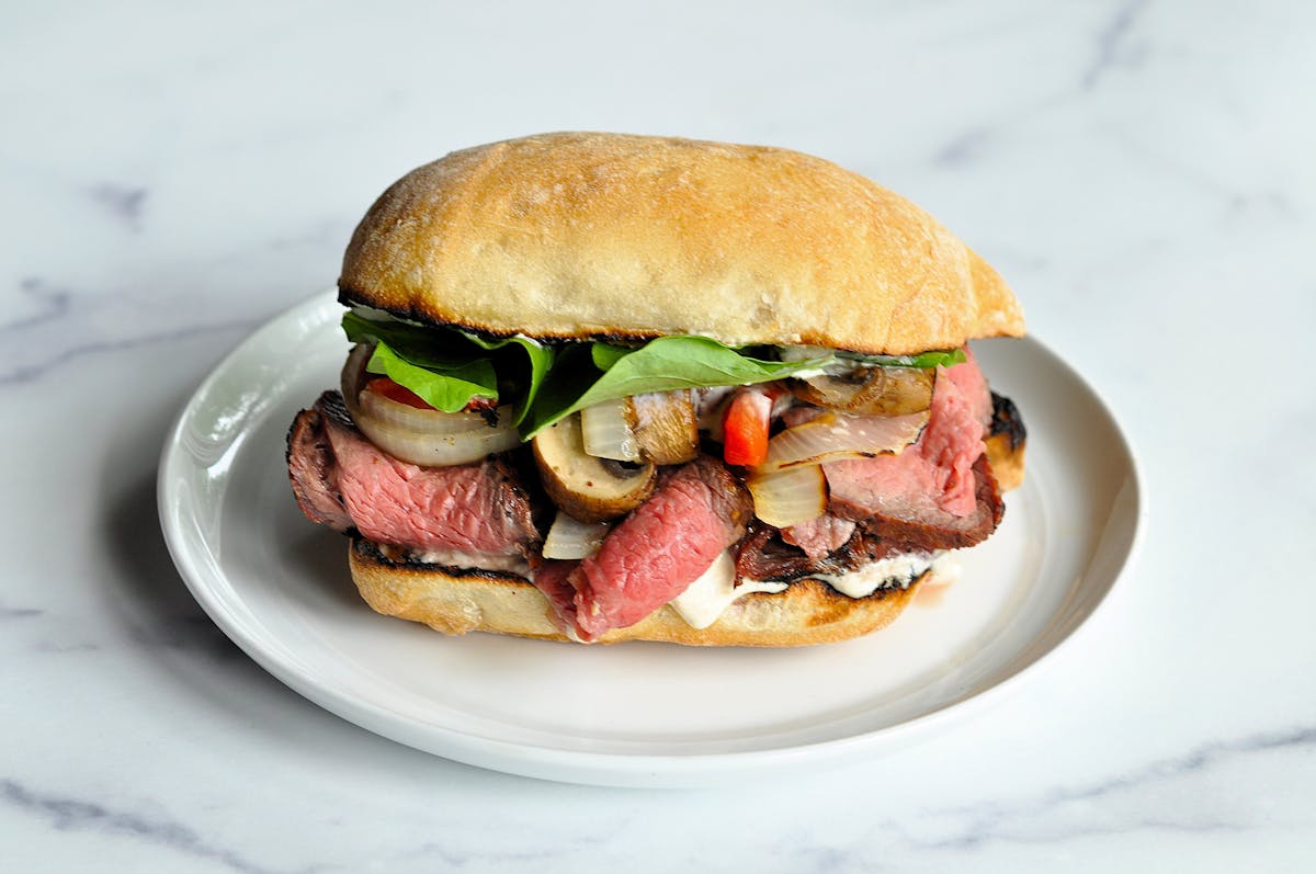 A ciabatta bun is stuffed with medium-rare tri-tip steak, mushrooms, peppers, onions and arugula, with a horseradish-mayo sauce.