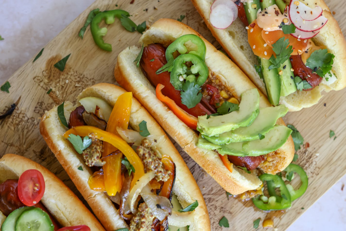 Hot dogs topped with a variety of toppings on a board for a summer gathering.