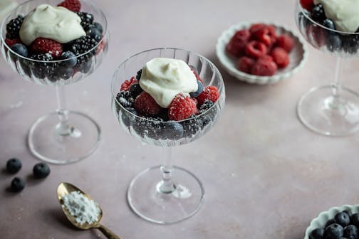 A glass is filled with fresh blueberries, raspberries and blackberries topped with a dollop of fresh ricotta.