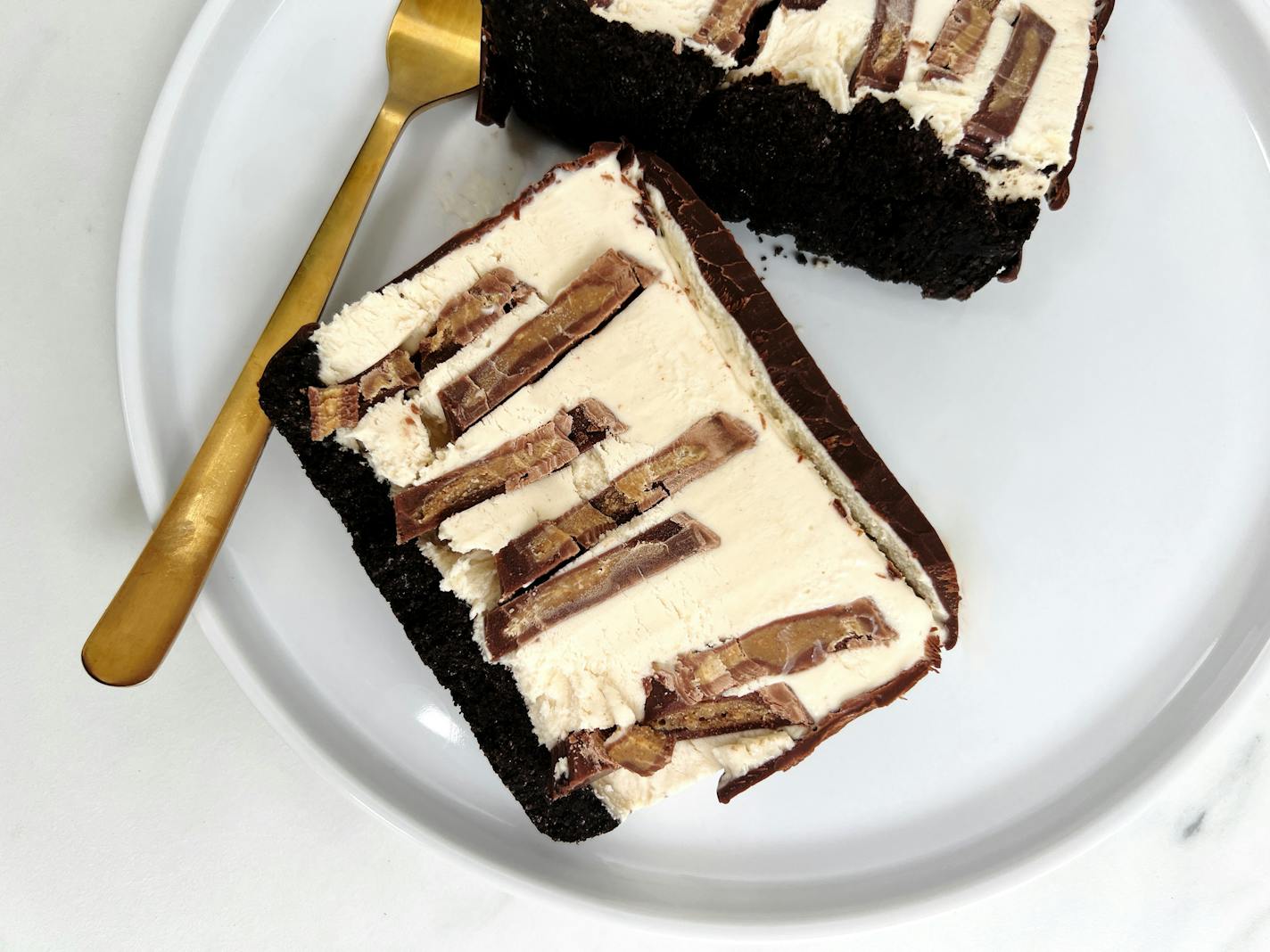 A slice of peanut butter ice cream cake on a plate, with an Oreo cookie crust and peanut butter cups throughout.