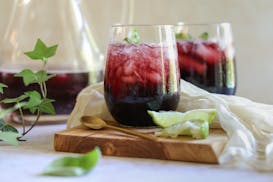 Two cocktail glasses with blueberry mojitos, garnished with mint leaves and lime wedges.