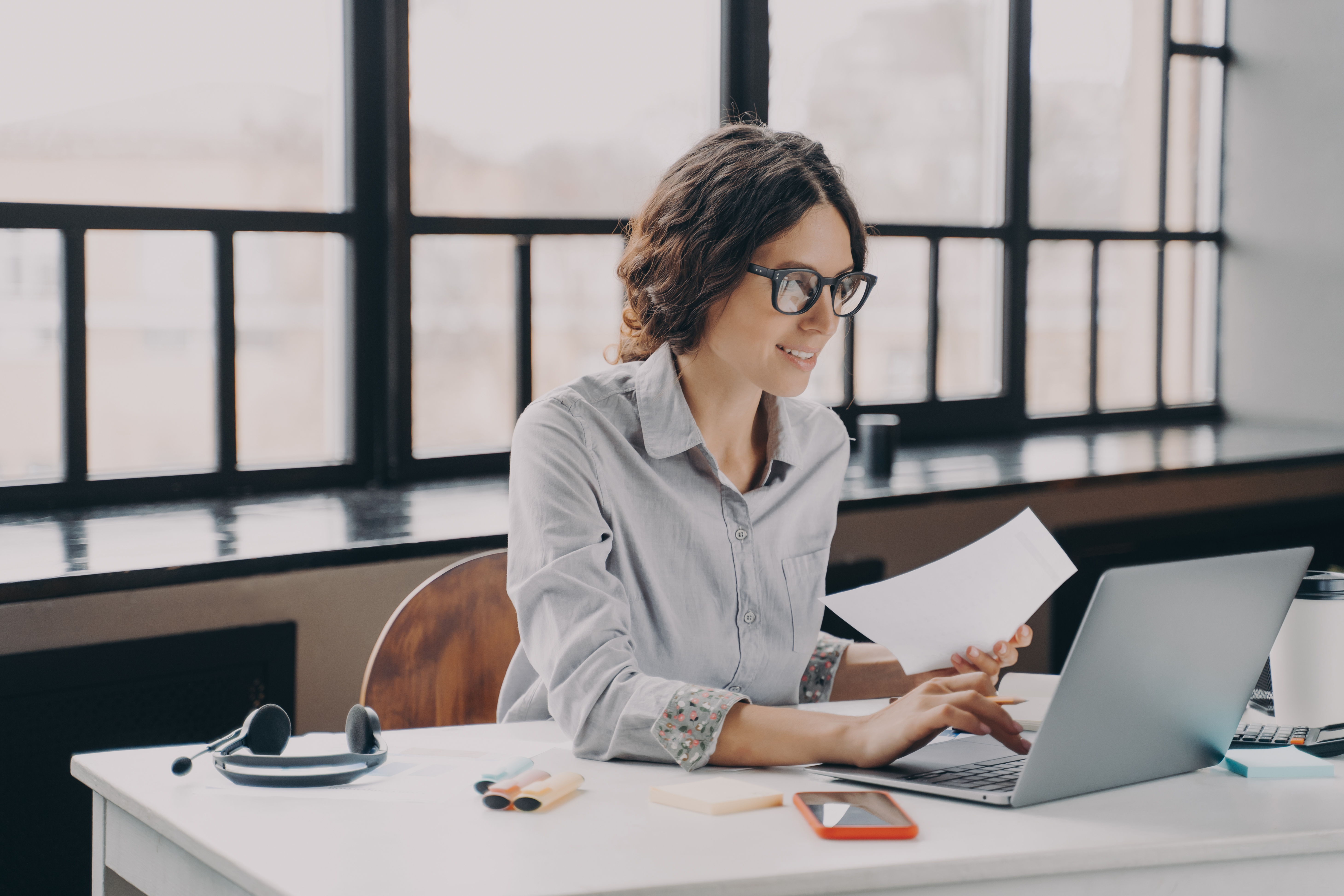 Woman working on laptop with paper in hand 