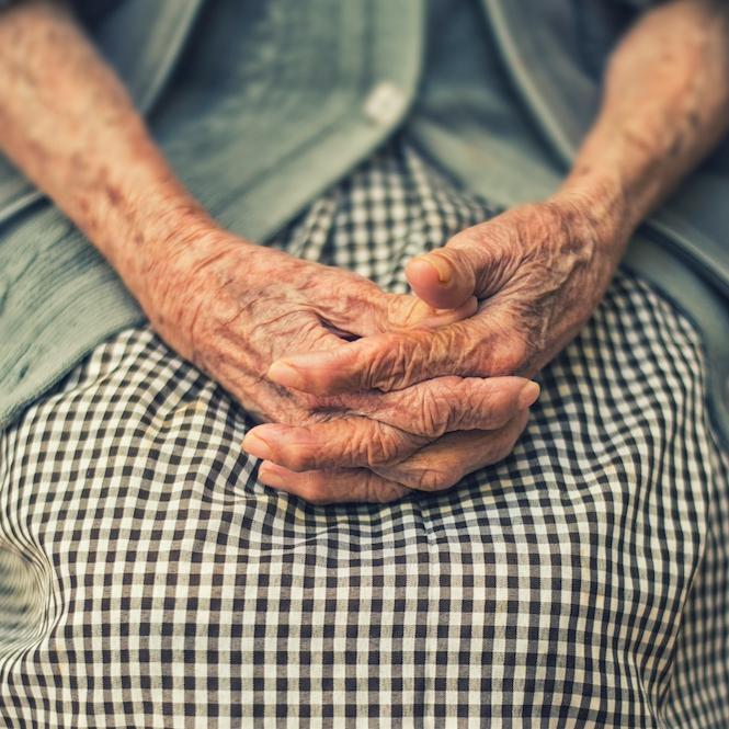 		Hands of an elderly person clasped on a gingham print skirt
	