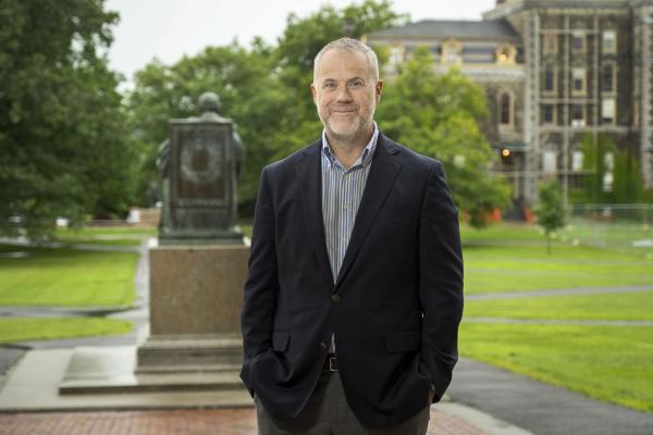 Dean Peter Loewen posing behind the A.D. White statue on the Arts Quad