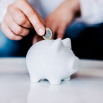 Person putting a coin in a small white piggy bank.