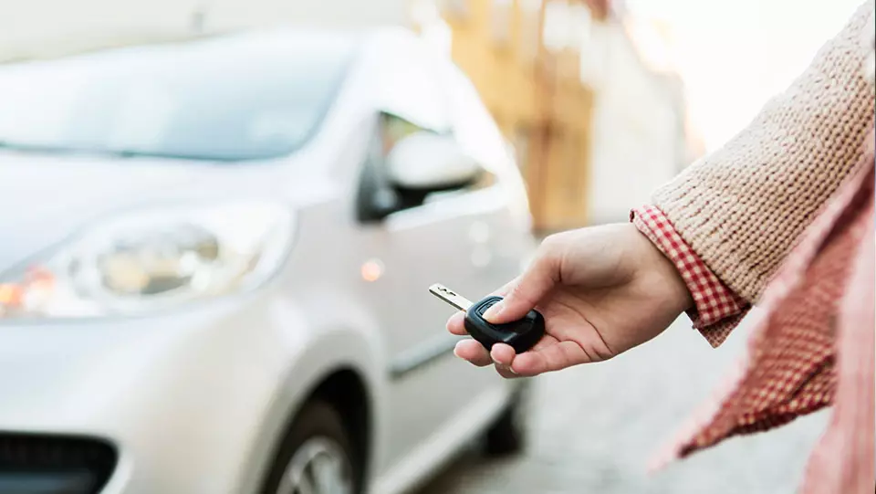 Woman using car key fob to lock car.