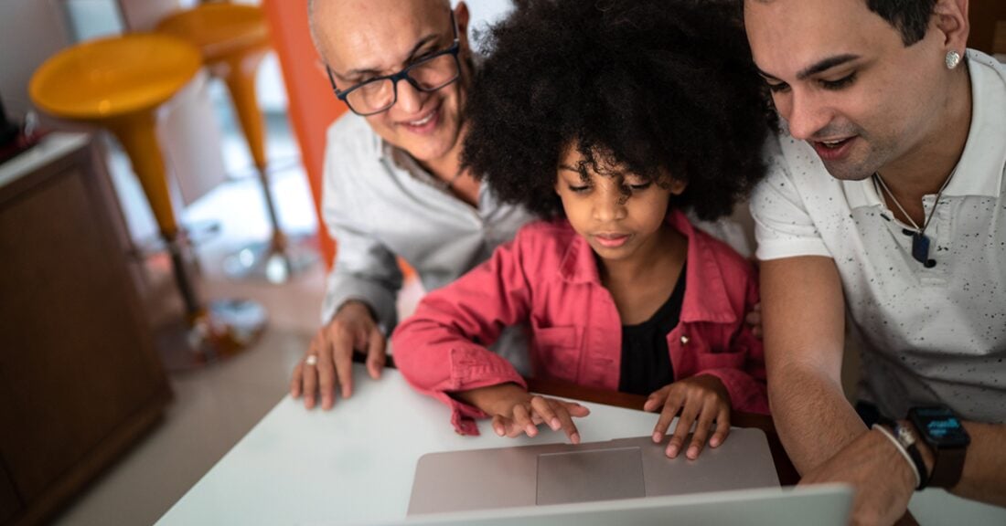 Two fathers sit with their young daughter in front of a laptop.