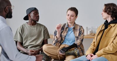 Three young people particpate in a grou therapy session with an adult leader.