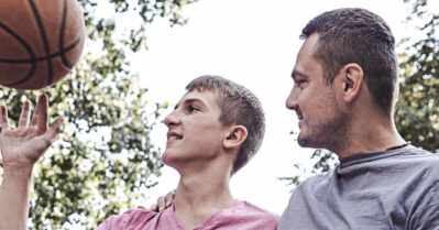 A young man plays basketball with an older male adult.