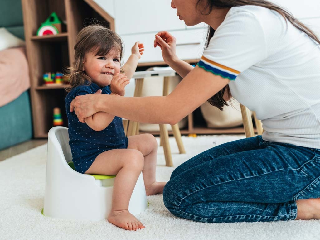 A toddler resisting sitting on a potty training seat