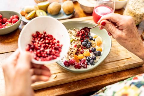 Hands scooping pomegranate seeds from bowl onto fruit bowl