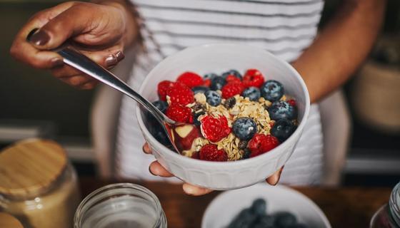 Person holding white bowl of healthy berries and oats, with spoon