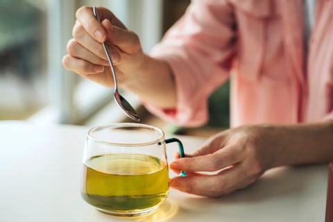 Person stirring glass mug of green tea with spoon