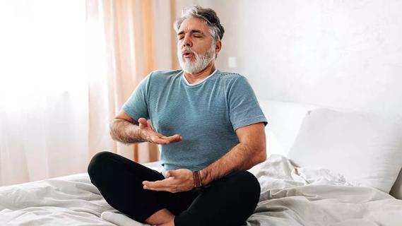 male doing yoga breathing exercises seated on a bed