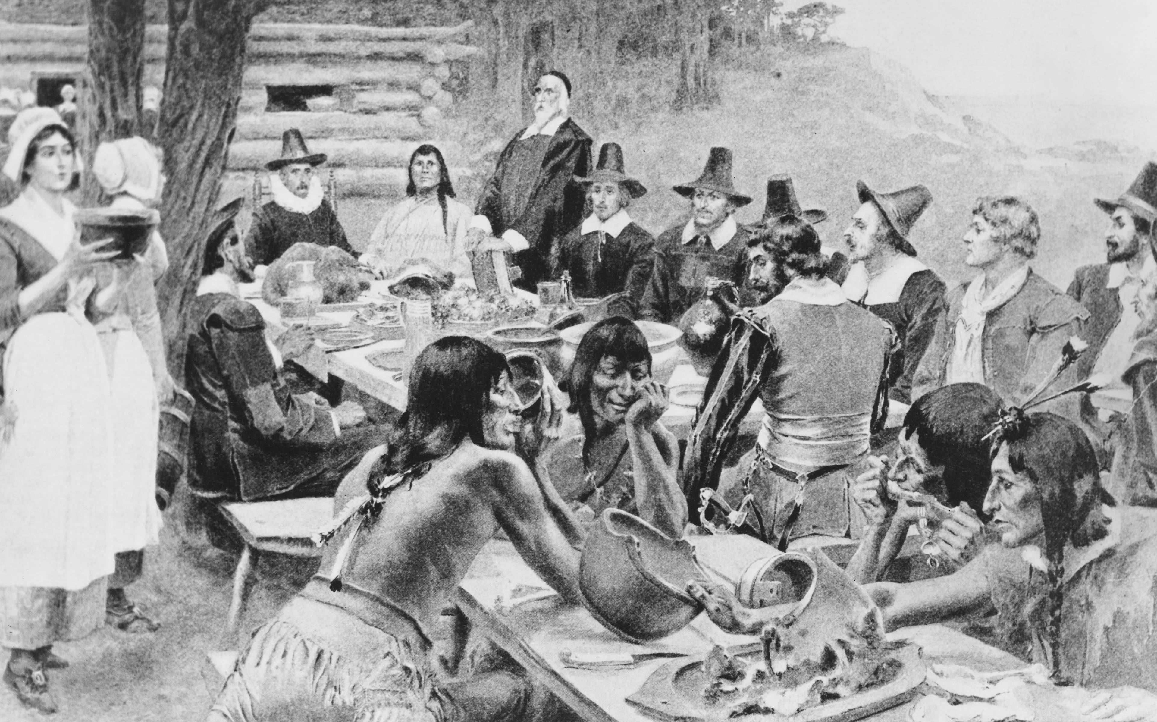 A depiction of early settlers of the Plymouth Colony sharing a harvest Thanksgiving meal with members of the local Wampanoag tribe at the Plymouth Plantation, Plymouth, Massachusetts, 1621.