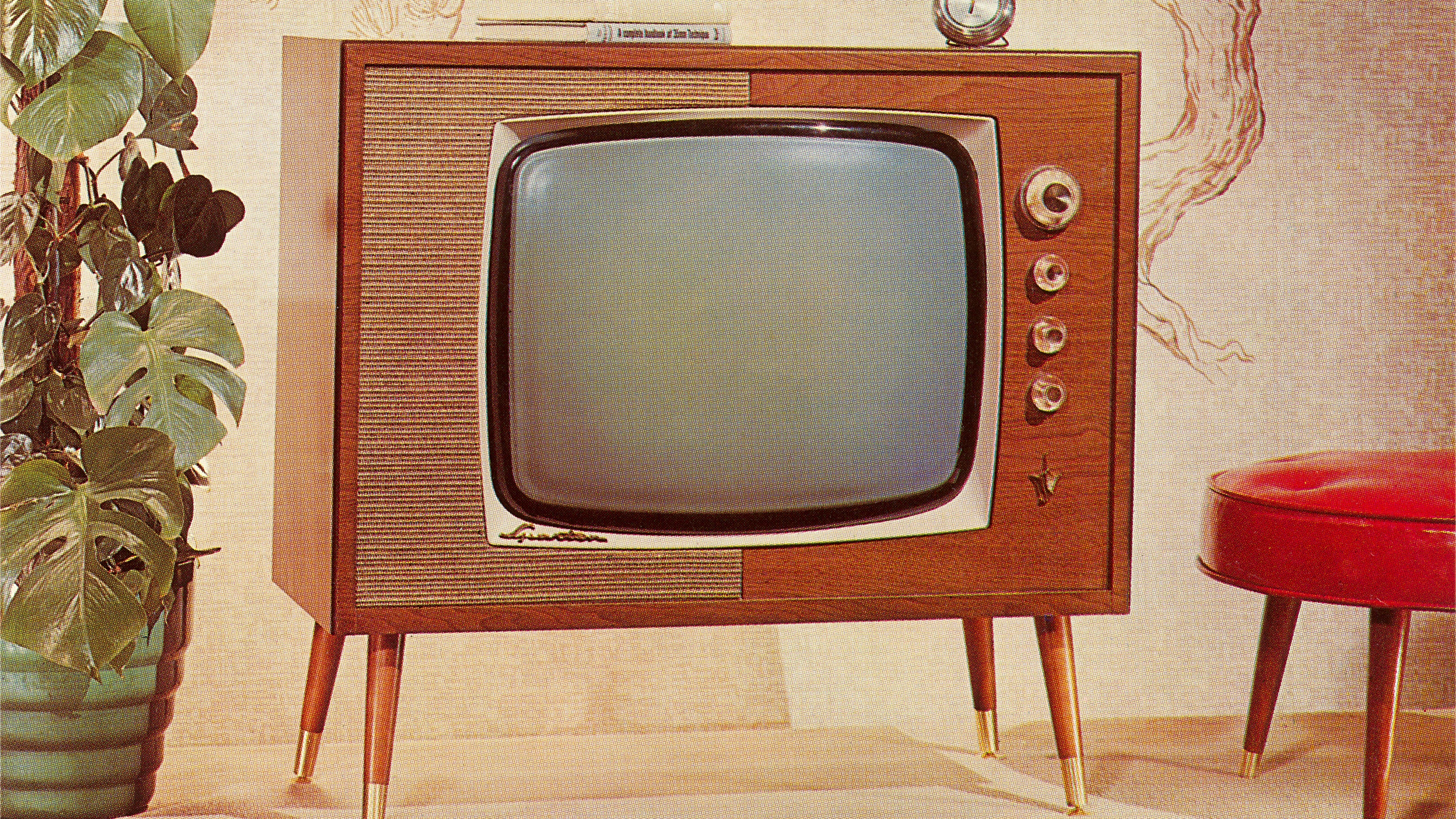 A 1960s-era TV set on legs is shown between a potted plant and red footstool.