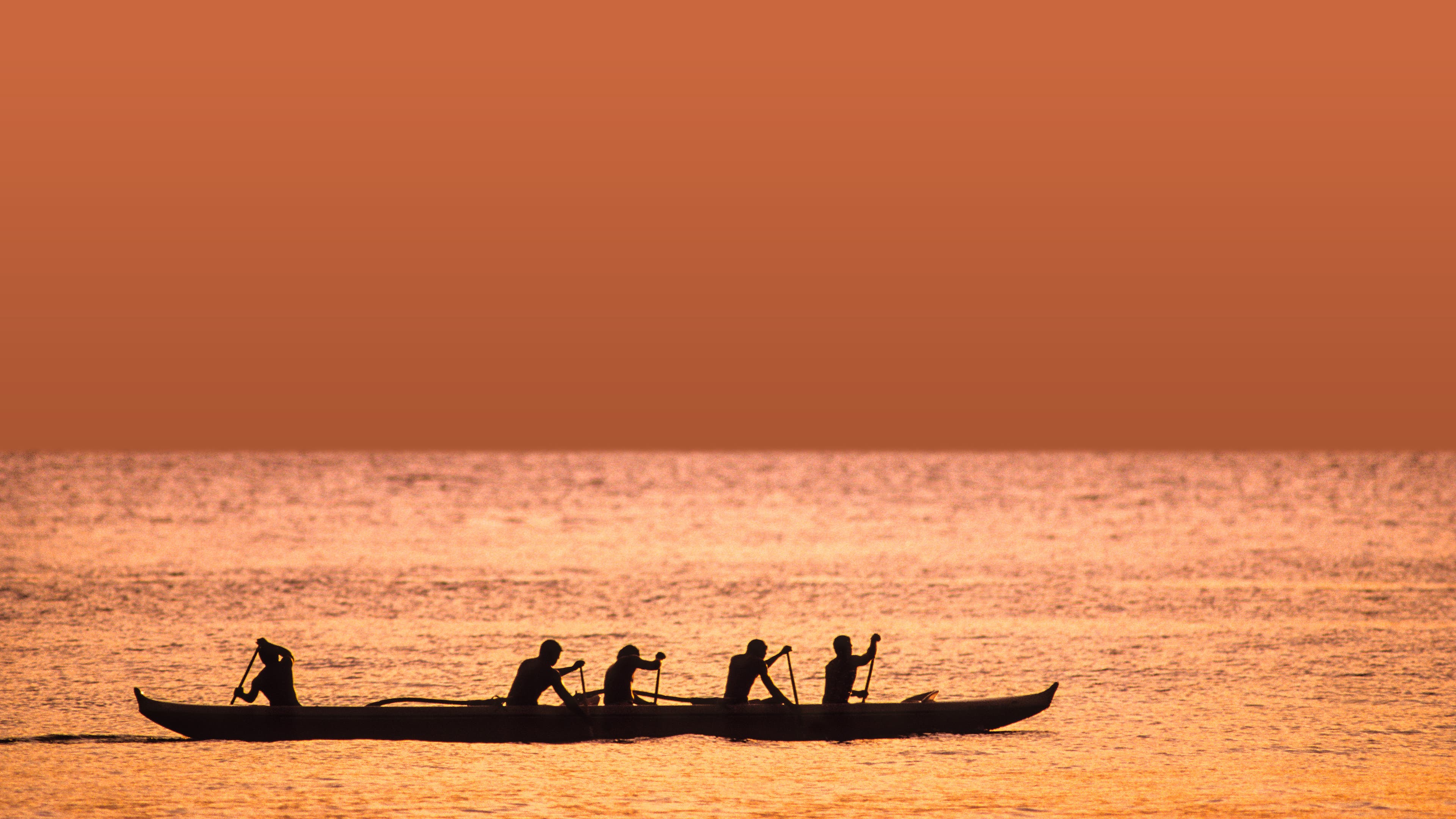 Hawaiian men paddling an outrigger canoe at sunset on the water